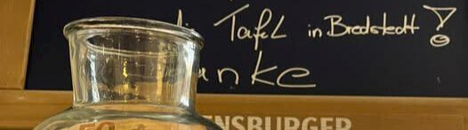 Glasflasche mit gesammeltem Geld vor Tafel mit Spendenaufruf